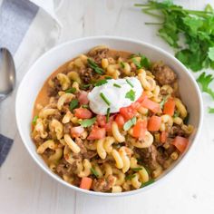 a white bowl filled with pasta and meat topped with sour cream, parsley on the side