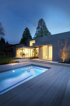 an outdoor swimming pool at night with lights on the windows and decking around it