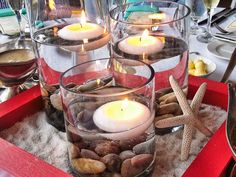 candles are lit in glass vases with rocks and starfish