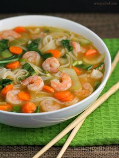 a bowl of shrimp noodle soup with carrots and spinach on a green napkin next to chopsticks