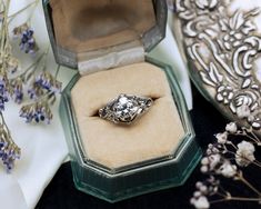 an engagement ring sits in a box next to some flowers and lavenders on a table