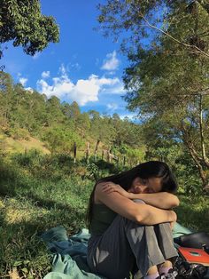 a woman is sitting on the ground with her arms folded over her head and looking into the distance