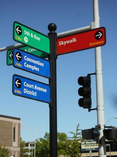 street signs pointing in different directions on a pole with traffic lights and buildings in the background