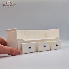 a hand is holding a miniature model of a house with three doors and four drawers