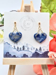 a pair of blue heart shaped earrings sitting on top of a easel next to flowers