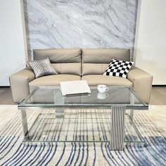 a glass coffee table sitting on top of a rug in front of a couch with pillows