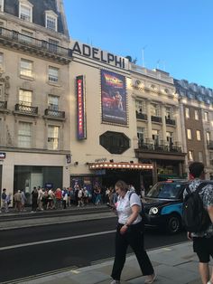 people are walking on the sidewalk in front of a building with an adelphi sign