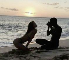 a man and woman are sitting on the beach while one takes a photo with a camera