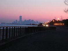 the city skyline is lit up at night as seen from across the water in front of a bridge