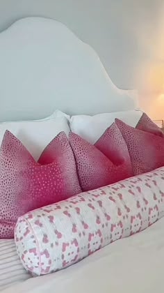 a white bed with pink pillows and a large pillow on it's headboard