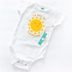 This bright and cheerful "Lil Ray Of Sunshine" baby onesie is made in the USA from 100% organic cotton and features a lapped neckline and 3 metal snaps for easy on/off diaper changes. You won't be able to resist the urge to smile when you see your little one snuggled up in this adorable onesie! Available in sizes 0-3M, 3-6M, 6-12M, and 12-18M. Shades of yellow, Orange and White. Vinyl heat transfer print. Each baby onesie is proudly sewn in the USA and is joyfully printed in small batches by Sun Sunshine Artwork, Gender Neutral Outfit, Contoured Burp Cloth, Ray Of Sunshine, Newborn Hat, Organic Cotton Baby, Receiving Blankets, Baby Gift Sets, Shades Of Yellow