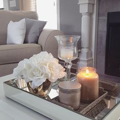 candles and flowers on a tray in front of a fire place with a couch behind it