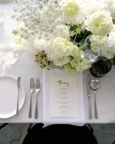 the table is set with white flowers and silverware