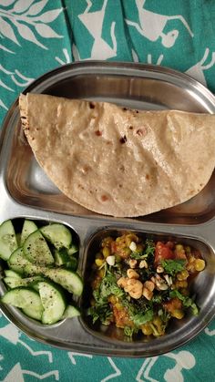 a metal tray filled with food on top of a blue and white table cloth next to cucumbers