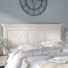 a clock on the wall above a bed in a room with blue walls and white furniture