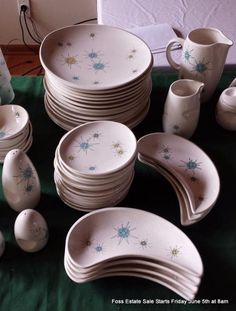 a table topped with lots of white dishes and cups on top of a green cloth