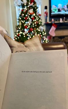 an open book sitting in front of a christmas tree