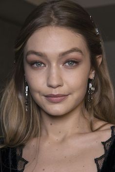 a woman with long hair and blue eyes wearing earrings on her head, looking at the camera