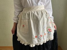 a woman wearing a white shirt and black skirt with red flowers on the bottom, standing in front of a wall