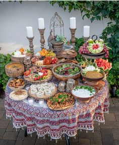 a table topped with lots of different types of food next to tall candles and greenery