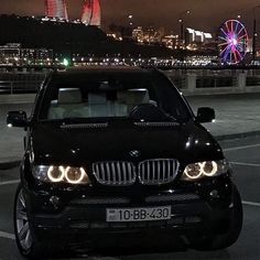 a black car parked in front of a ferris wheel with the city lights in the background