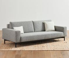 a gray couch sitting on top of a wooden floor next to a white wall in a living room