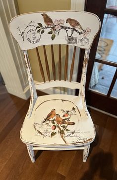 a white chair with birds painted on the back and sides, sitting in front of a door