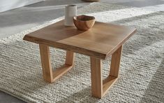 a wooden table sitting on top of a white rug next to a vase and cup