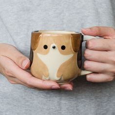 a woman holding a coffee mug with a dog on it's side and her hands in the cup