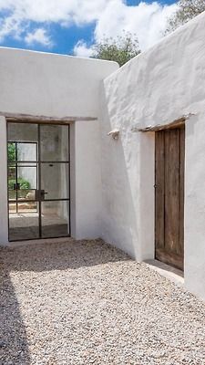 an adobe style house with two doors and gravel ground