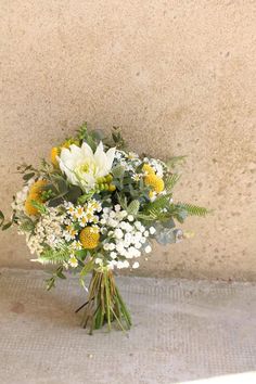 a bouquet of white and yellow flowers in front of a stone wall with concrete flooring