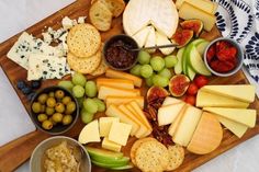 an assortment of cheeses, crackers and fruit on a wooden platter