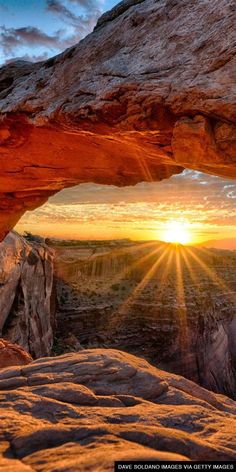 the sun is shining through an arch in the rock formation, with rocks below it