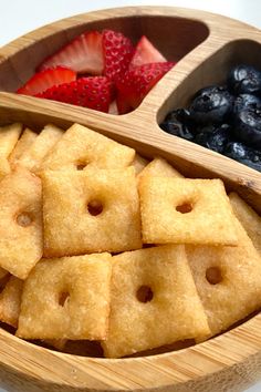 a wooden bowl filled with blueberries, strawberries and crackers on top of a table