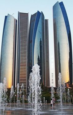 several tall buildings with fountains in front of them