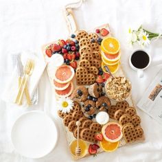 a table topped with waffles, orange slices and fruit next to a cup of coffee