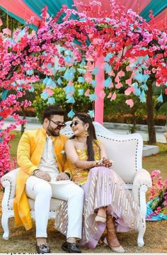 a man and woman sitting on a white couch under a canopy with pink flowers in the background