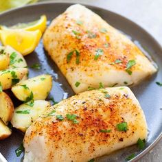 two fish fillets on a plate with potatoes and lemon wedges