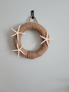 a rope wreath with starfishs hanging from the side on a gray wall next to a black hook