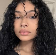 a woman with black curly hair and piercings on her nose is looking at the camera