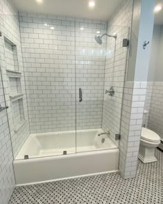 a white tiled bathroom with a walk in shower next to a toilet and bathtub