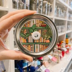 a person holding up a tin with a design on it in front of shelves full of books