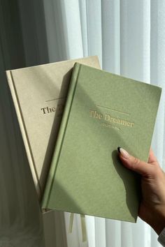 a person holding two books in their hands, one is green and the other is beige