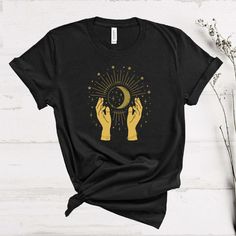 Mystic Moon Shirt, Moon T-Shirt, Magic Hands Shirt, Boho Vintage Moon Shirt, Faith Shirt, Spiritual T-Shirt, Woman Shirt, Celestial Tshirt Welcome to AuroraConceptDesign! ❤️ 👉🏻 PROCESSING TIME: - 3-5 business days. - Please contact with us if there is a rush order. 👉🏻 DELIVERY TIME: - Standard Shipping:  3-5 business days - Expedited Shipping  1-3 business days 👉🏻 CARE INSTRUCTIONS: - Machine wash cold and tumble dry low.  - Do not iron directly onto the design. - Do not bleach. We offer wide variety of products, including Unisex T-shirts, Women's V-neck T-shirts, Unisex Long Sleeve T-shirts, Youth T-shirts, Toddler T-shirts, and many more. Swipe listing images and check all the colors available for each type of shirt. Please enter the shirt and text color desired for your shirt in t Mystical Cotton Crew Neck T-shirt, Mystical Crew Neck Cotton T-shirt, Mystical Graphic Print Crew Neck Top, Mystical Style Cotton T-shirt With Crew Neck, Mystical Style Cotton Crew Neck T-shirt, Black Crew Neck Top With Sun And Moon Design, Celestial Tshirt, Retro Collage, Mystic Moon