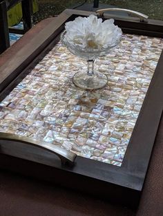 a glass vase sitting on top of a wooden table covered in mother of pearl tiles