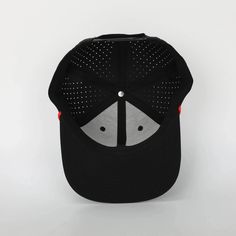 a black and grey baseball cap with holes on the front, two red pins at the peak