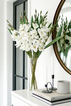 a vase with white flowers sitting on top of a table next to a mirror