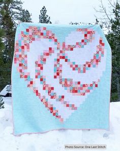 a heart shaped quilt hanging from the side of a snow covered tree line with trees in the background