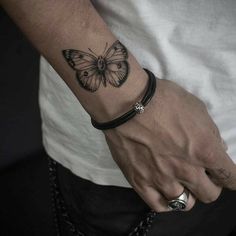 a man with a butterfly tattoo on his arm and wrist is wearing a black leather bracelet