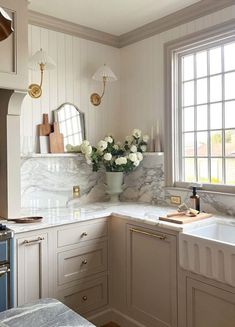 a white kitchen with marble counter tops and gold trim on the cabinets, sink, and window